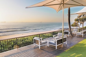 A deck with outdoor seating overlooking a beach and ocean. - Umhlanga Sands Resort by First Private Stays (Durban)