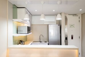 A compact kitchen with a microwave, refrigerator, sink, and pendant lights. - Umhlanga Sands Resort by First Private Stays (Durban)
