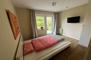 Ein Schlafzimmer mit einem Bett, einem Fenster, einer Heizung und einem Fernseher an der Wand.