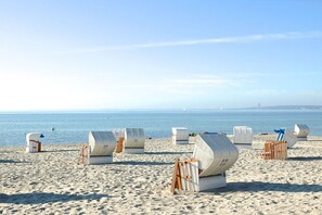 Ein Strand mit mehreren weißen Liegen und einer Holzbank.