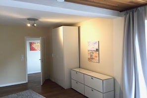 Quarto com teto de madeira, guarda-roupa branco, pequeno armário e um quadro na parede.