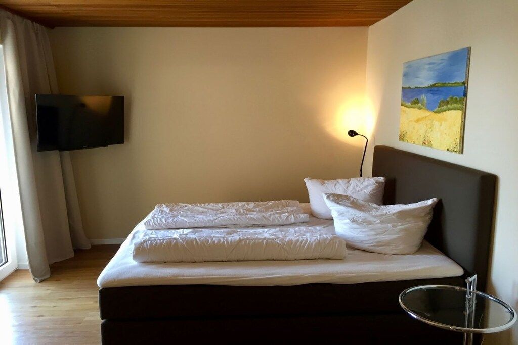 Un dormitorio con cama, televisor de pantalla plana en la pared, un cuadro y una mesita de noche.