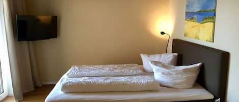Un dormitorio con cama, televisor de pantalla plana en la pared, un cuadro y una mesita de noche.