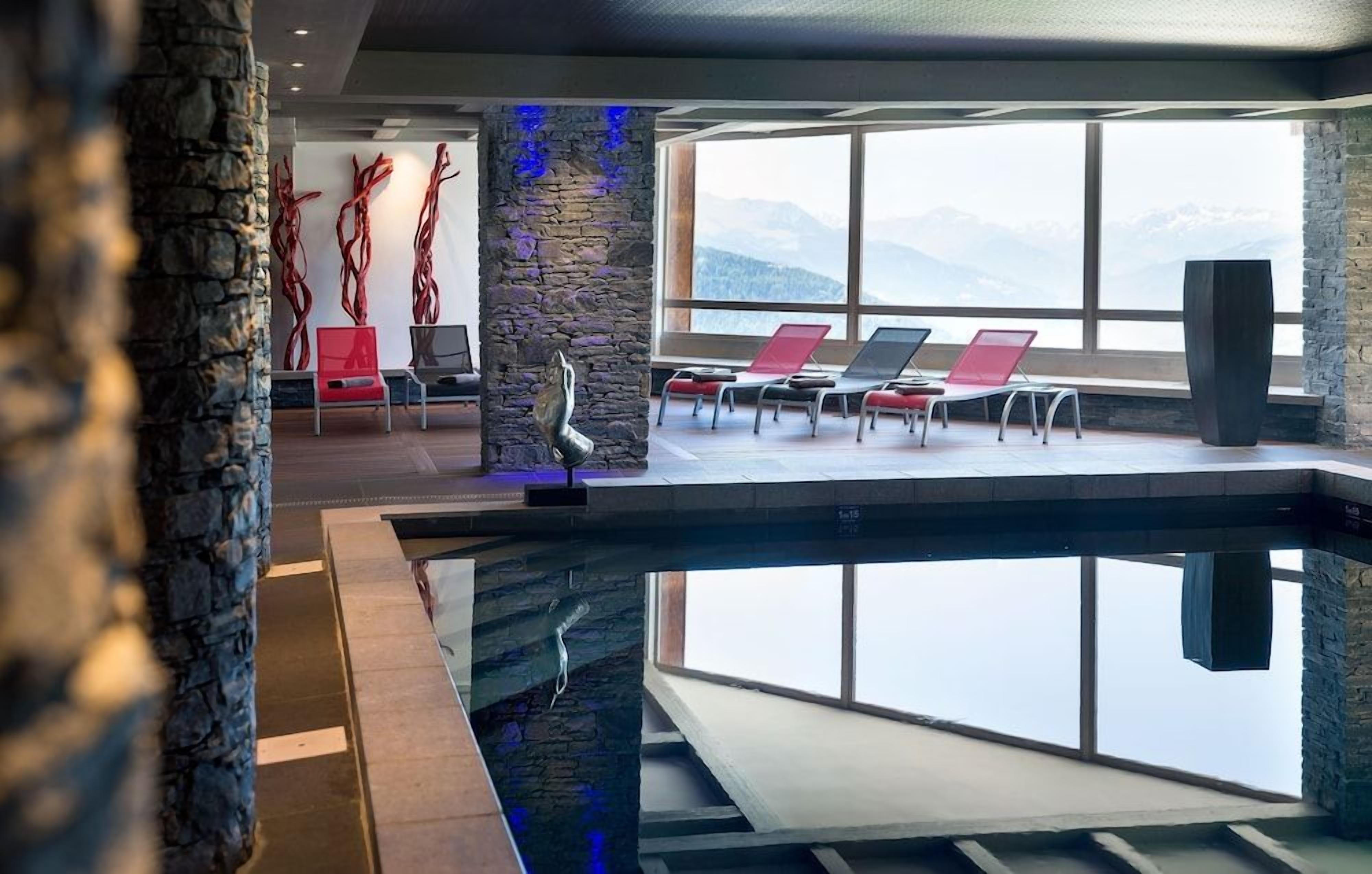 Un área de piscina moderna en el interior, con sillones de descanso y vistas a montañas.