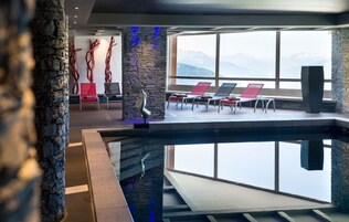 A modern indoor pool area with lounge chairs and a view of mountains.