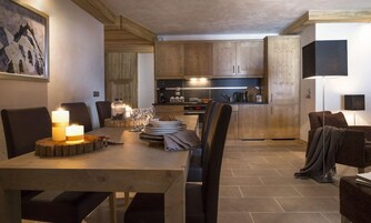 A modern kitchen with wooden cabinets, a dining table set for four, and a cozy seating area with a lamp.