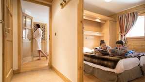 A room with a wooden floor, a bed with a fur throw, and a person reading a book. - Cgh Residences & Spas Le Lodge Hemera (Montvalezan)