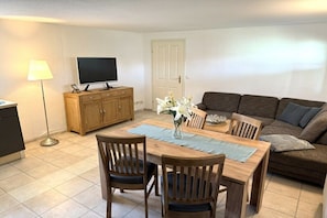 A living room with a wooden dining table, two chairs, a sofa, a television on a wooden cabinet, and a lamp. - Holiday home in Ketzin with swimming pool (Ketzin)