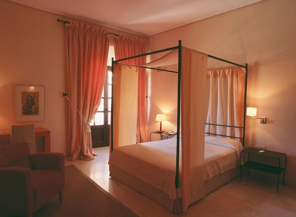 Una cama con dosel y cuatro columnas, una mesita de noche, una silla y una lámpara.