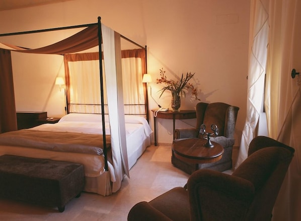 A four-poster bed with a canopy, a sitting area with a round table, and a small side table with a vase of flowers.