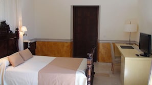 Una habitación de hotel con cama, escritorio, silla, lámpara y una puerta.