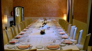 Una larga mesa de comedor dispuesta para una comida formal, con múltiples sillas, mantel blanco y una disposición simétrica de platos, copas y cubiertos.