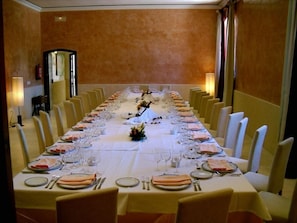 A long dining table set for a formal meal with multiple chairs, a white tablecloth, and a symmetrical arrangement of plates, glasses, and cutlery.