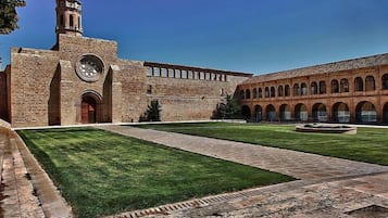 Un cortile con un edificio caratterizzato da una torre dell'orologio e finestre ad arco.