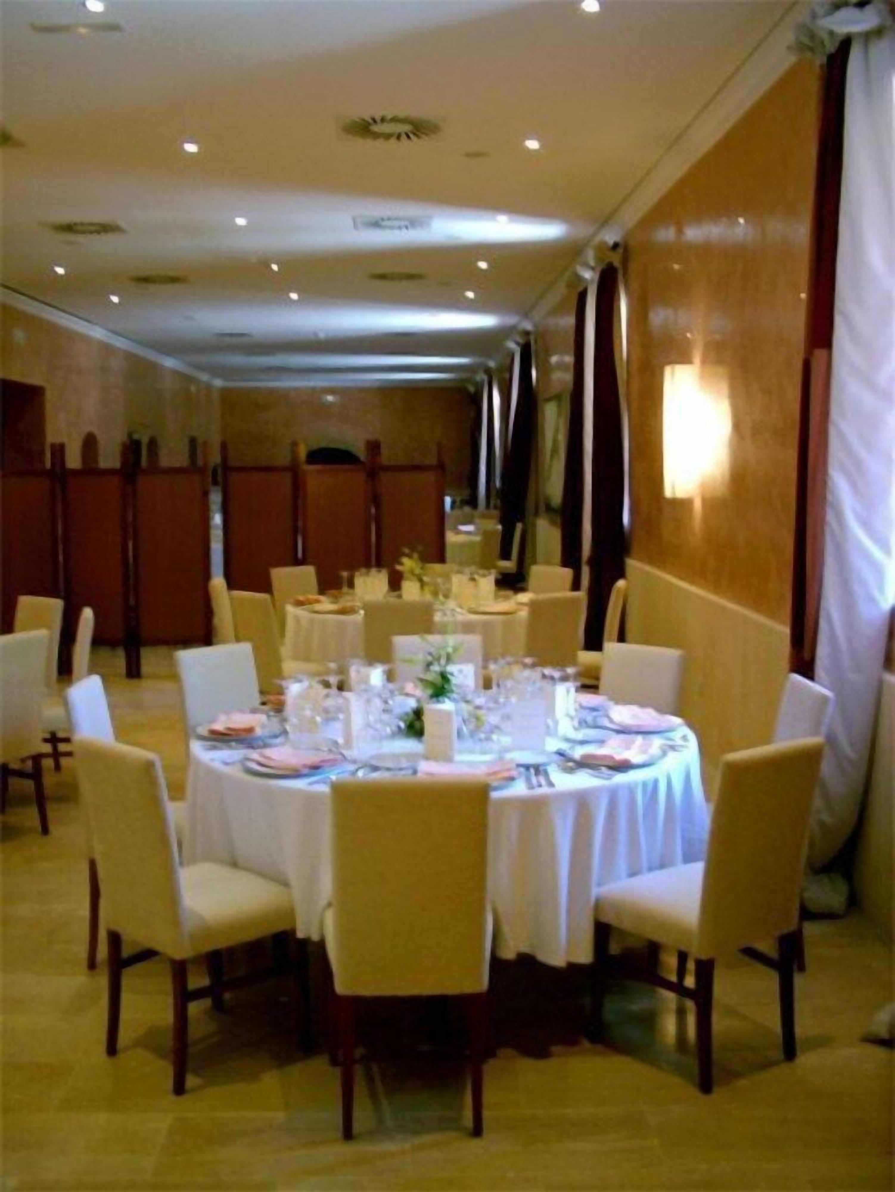 Une salle de banquet avec des tables rondes dressées pour le repas, des chaises et une longue table en arrière-plan.