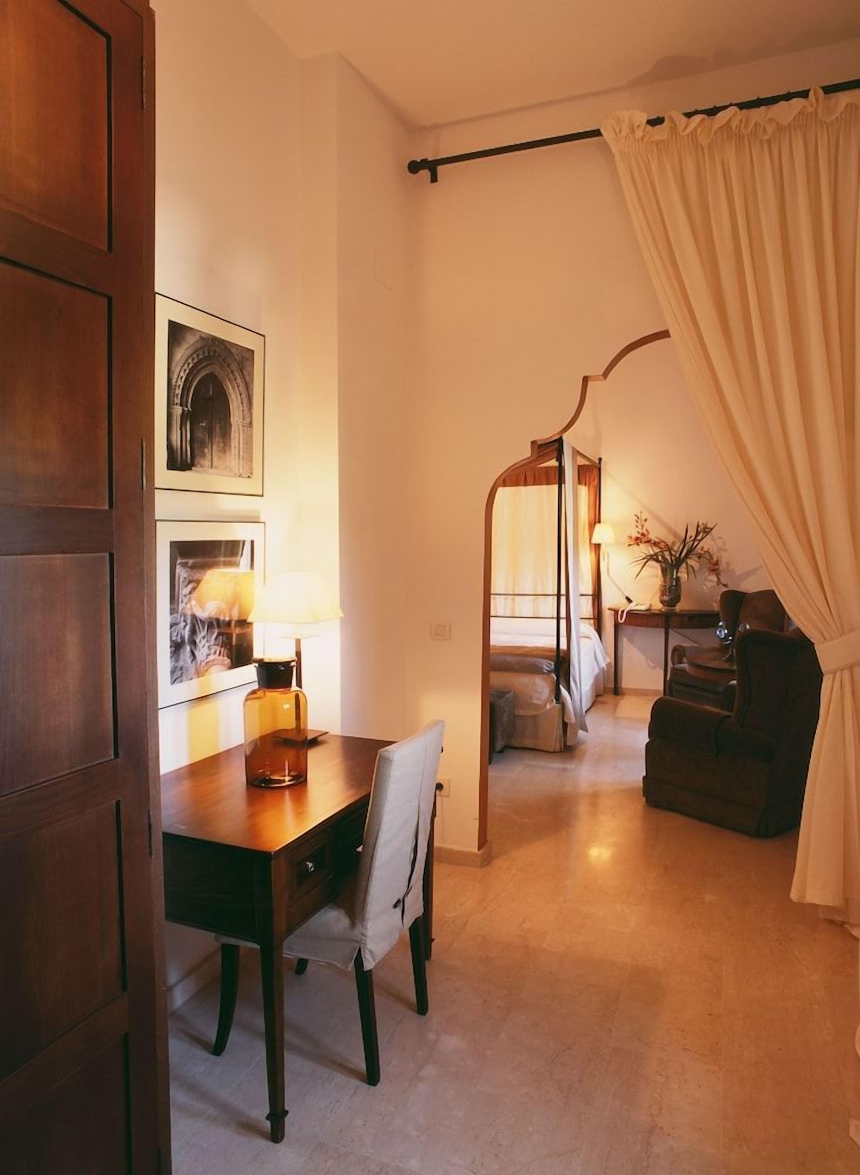 Une chambre d’hôtel comprenant une table à manger, une chaise, un lit à baldaquin, un bureau avec une lampe et une autre chaise.