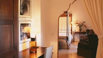 Une chambre d’hôtel comprenant une table à manger, une chaise, un lit à baldaquin, un bureau avec une lampe et une autre chaise.