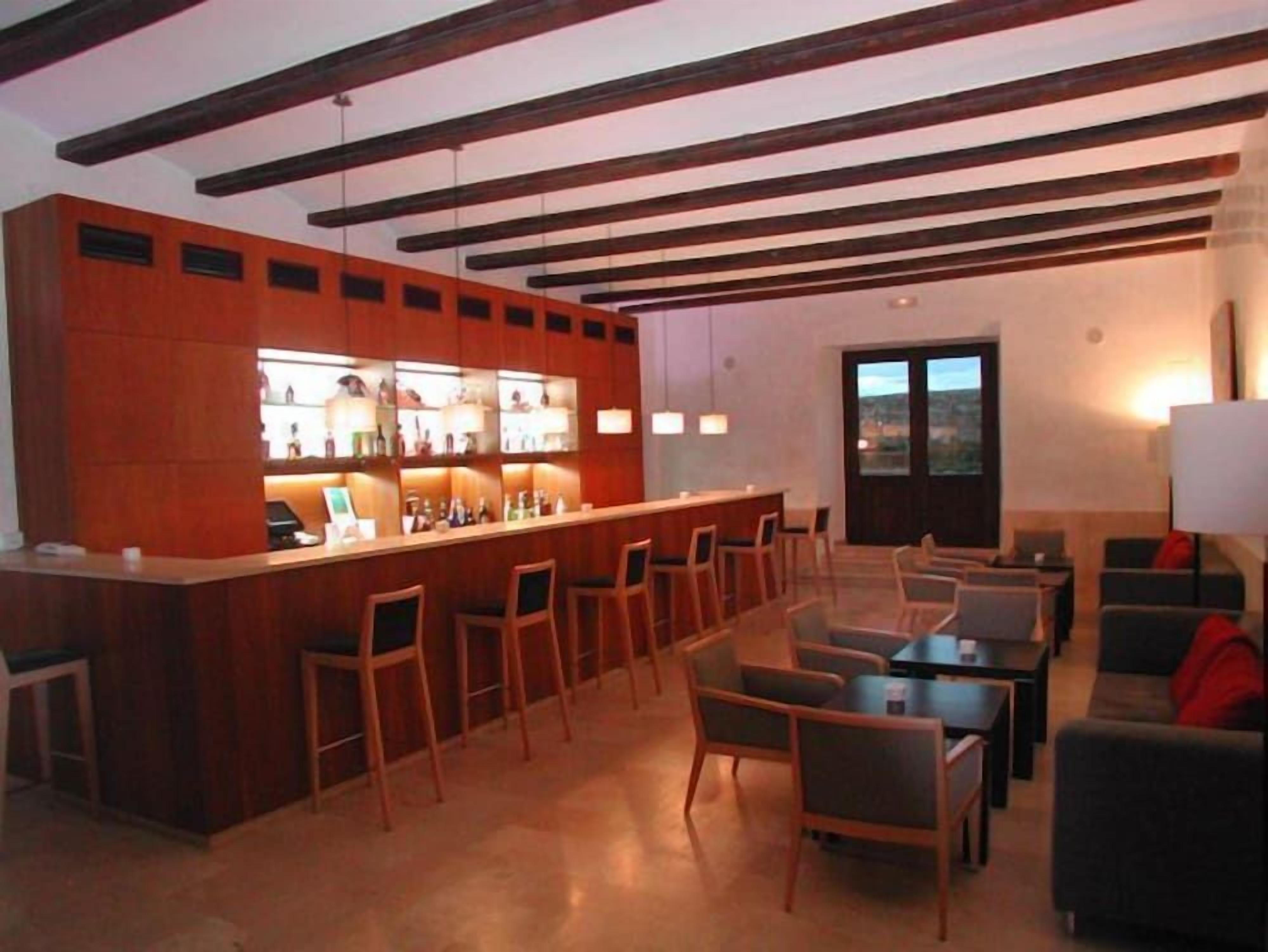 Un área de bar con sillas y mesas de madera, una barra con botellas y una vista a través de una puerta.