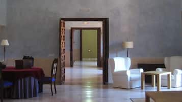 Hall d'albergo con area ristorazione, posti a sedere e un corridoio che porta in un'altra stanza.