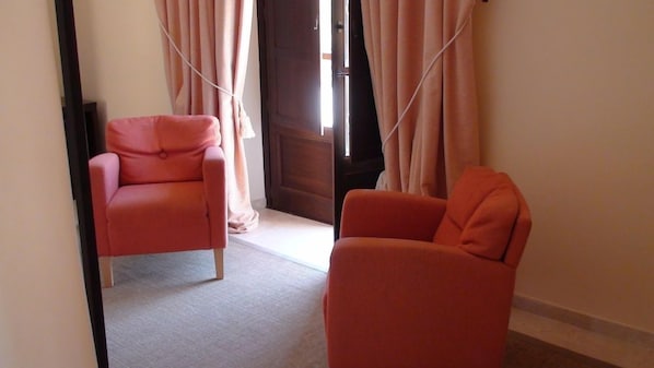 Una habitación con dos sillas anaranjadas, una puerta de madera y cortinas de color claro.