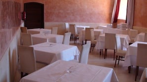 Un área de comedor con varias mesas y sillas, un extintor en la pared y una ventana con cortinas.