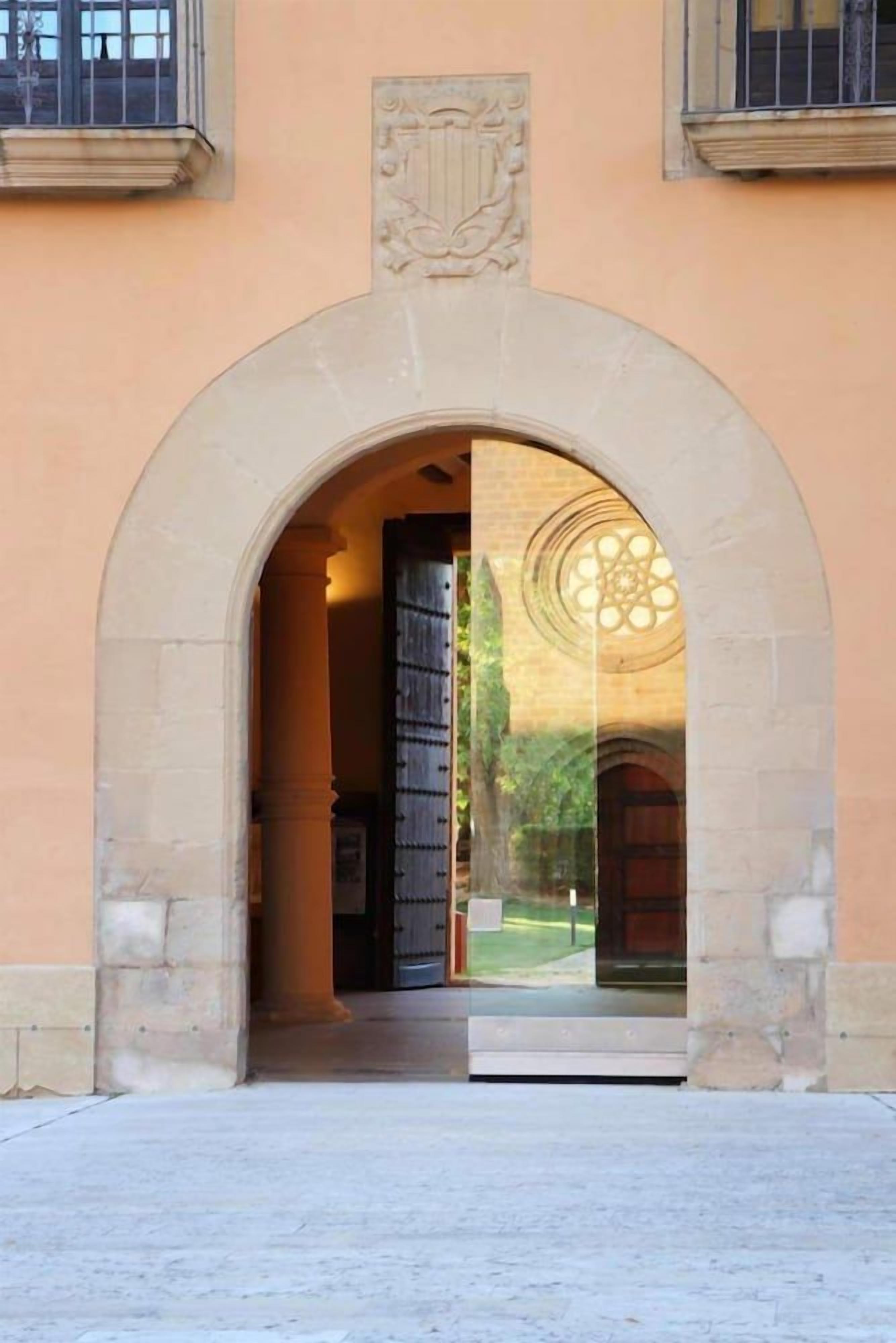 An arched entrance with a stone facade, a door, and a window with a geometric pattern.