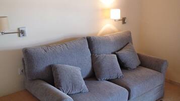 Un sofá gris con cuatro cojines en una habitación con un aplique de pared.