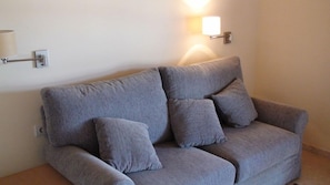 A grey sofa with four cushions in a room with a wall-mounted light fixture.