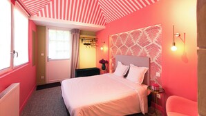 Een slaapkamer met een bed, nachtkastje, wandlamp en een raam met gordijnen.