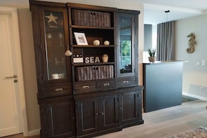 A dark wooden cabinet with glass doors, shelves with decorative items, and a word 'SEA' on one shelf. - Residence by the sea - Strandallee 178 (Timmendorfer Strand)