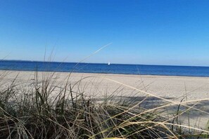A beach with a clear sky, a sandy shore, and a sailboat in the distance. - Residence by the sea - Strandallee 178 (Timmendorfer Strand)