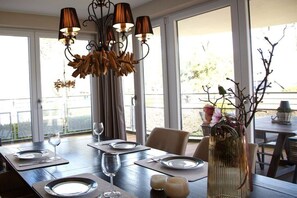 A dining area with a table set for four, a decorative chandelier, and a view through large windows. - Residence by the sea - Strandallee 178 (Timmendorfer Strand)
