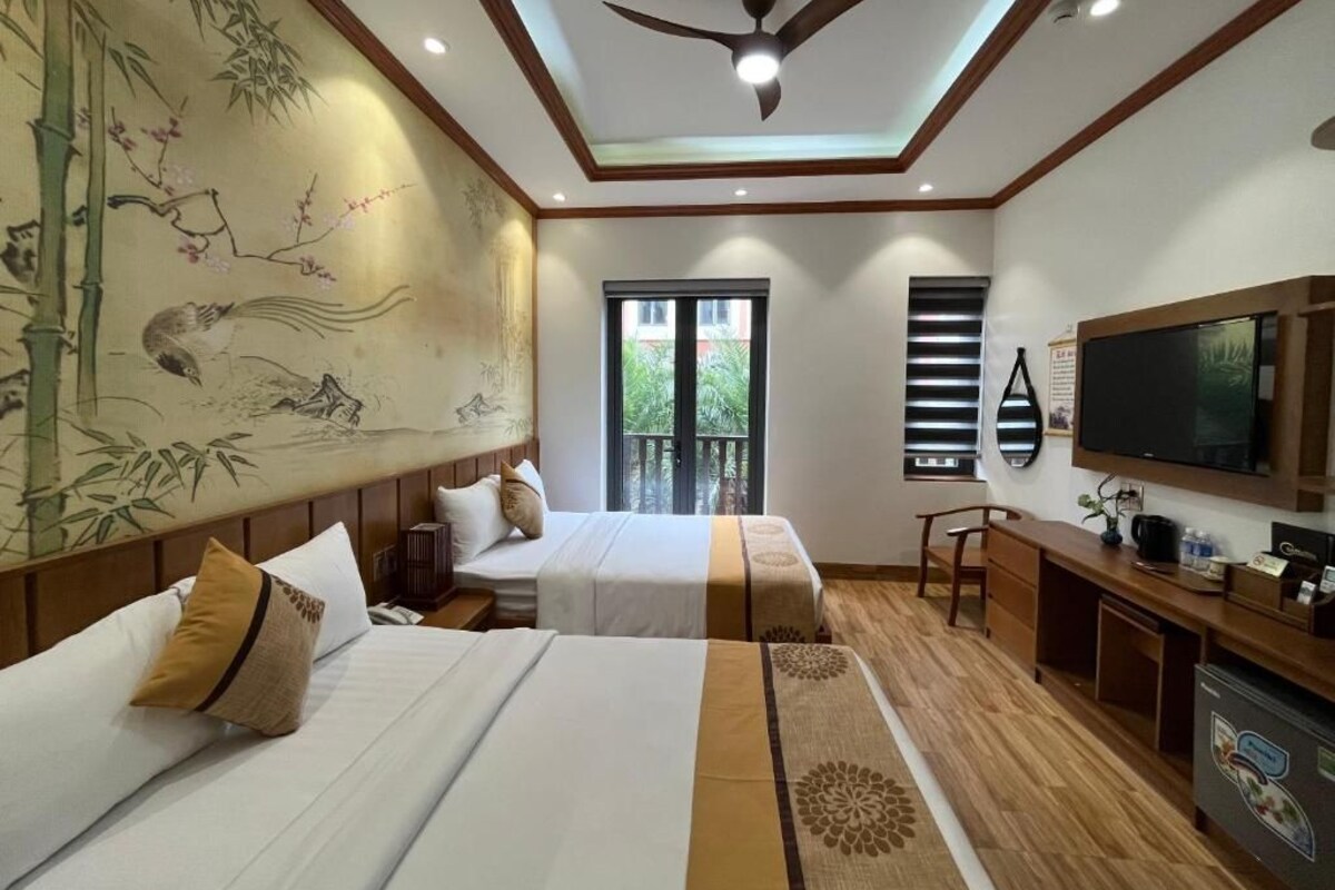 A hotel room with two beds, a ceiling fan, a television, and a large window.
