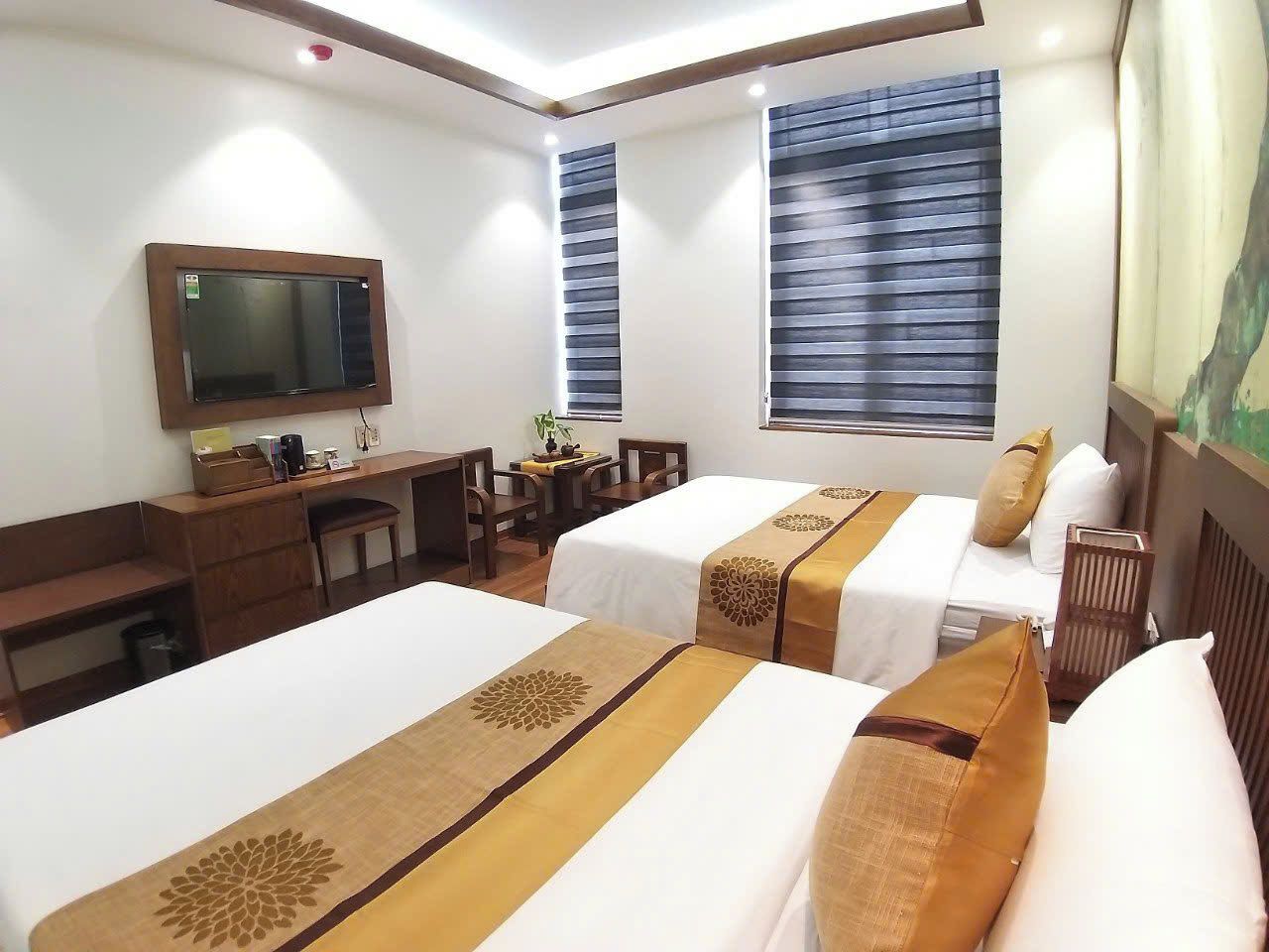 A hotel room with two beds, a desk, a chair, a television, and a window with blinds.