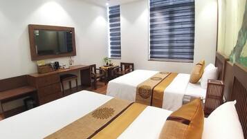 A hotel room with two beds, a desk, a chair, a television, and a window with blinds.