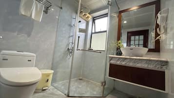 Un baño moderno con ducha envuelta en vidrio, inodoro, lavamanos con encimera de mármol y espejo.