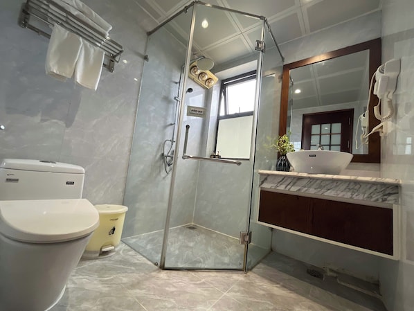 Un baño moderno con ducha envuelta en vidrio, inodoro, lavamanos con encimera de mármol y espejo.