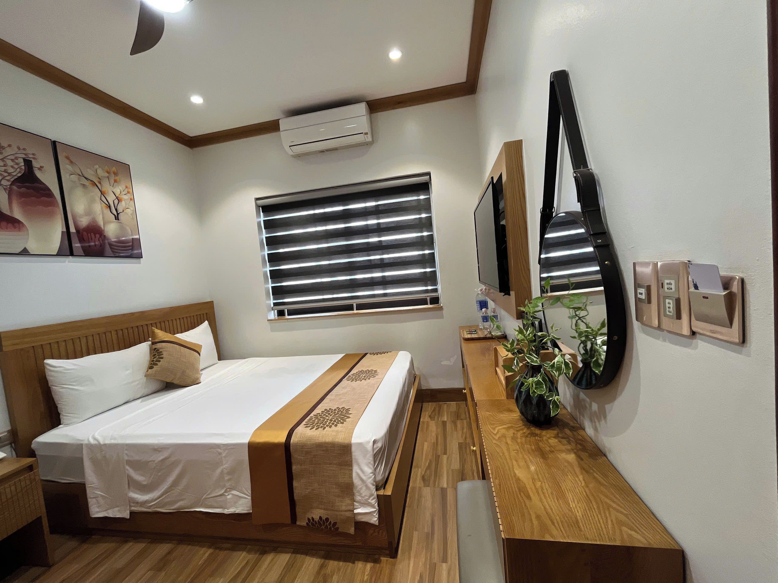 Une chambre d’hôtel comprenant un lit, une table de chevet, un climatiseur fixé au mur, une fenêtre avec stores et un téléphone fixé au mur.