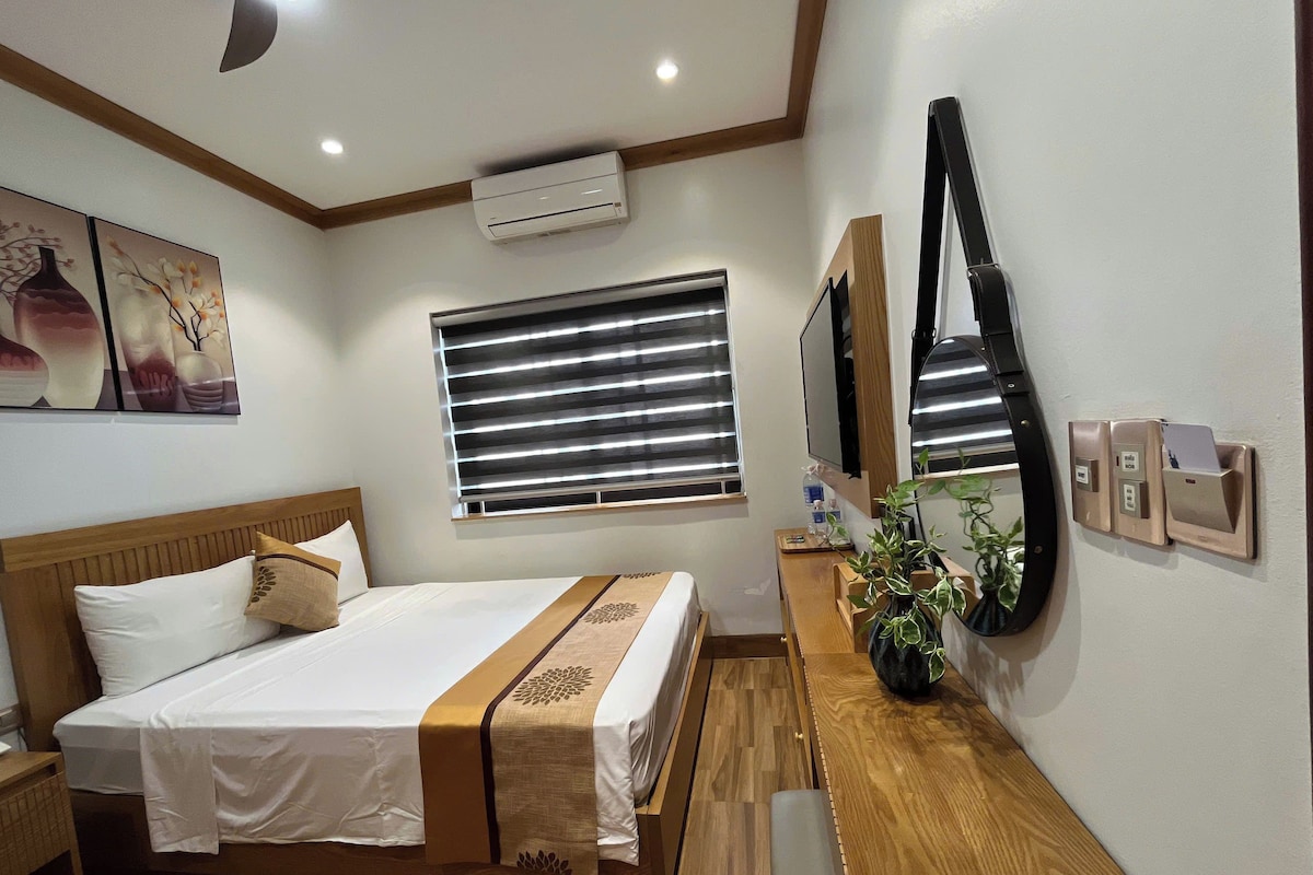 Habitación de hotel con cama, mesita de noche, aire acondicionado de pared, ventana con persianas y teléfono de pared.