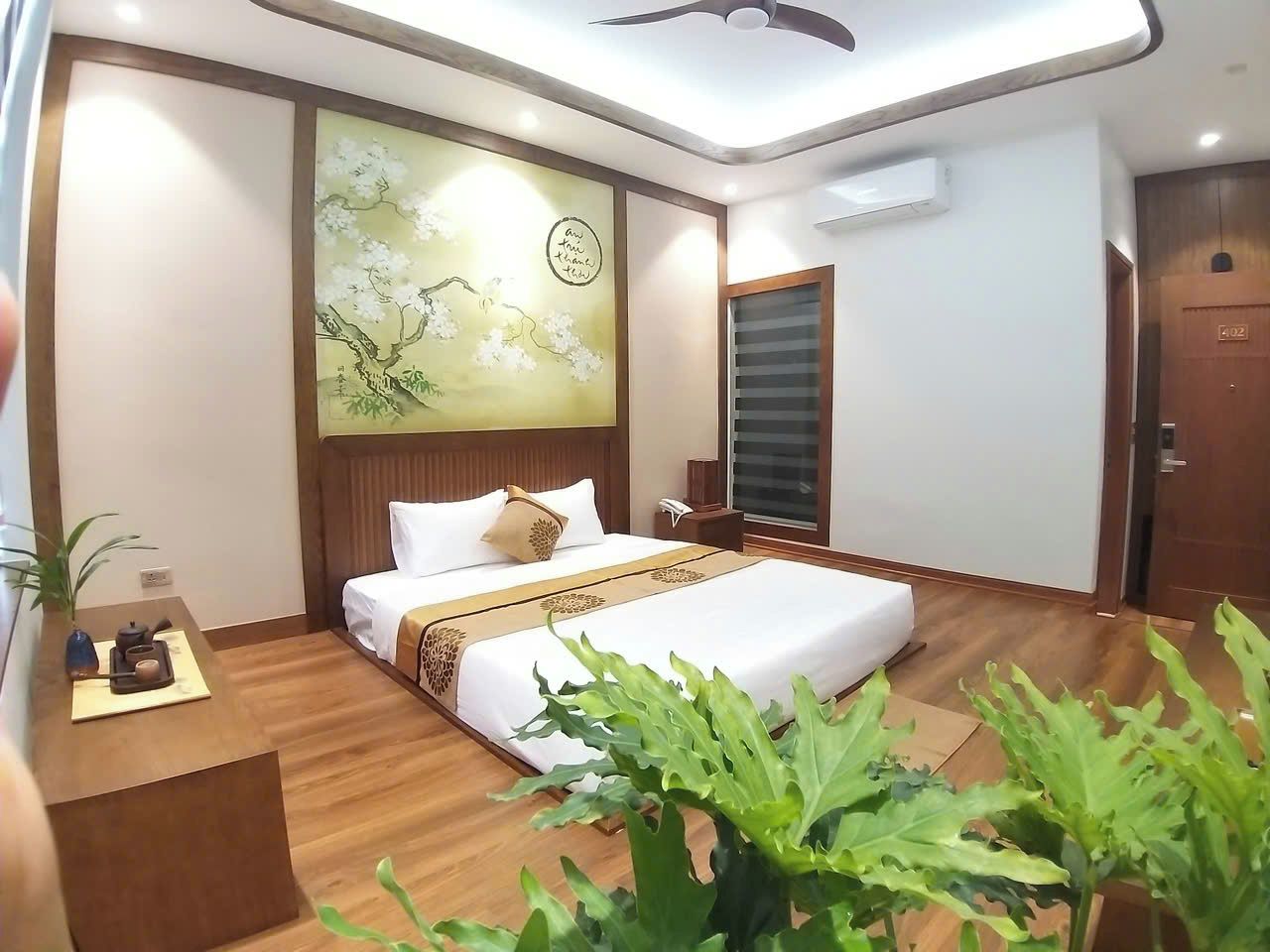 A hotel room with a bed, bedside table, and a wall with a floral painting.