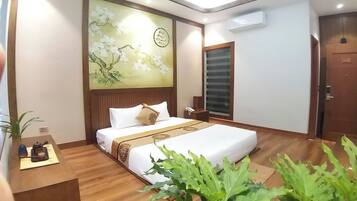 A hotel room with a bed, bedside table, and a wall with a floral painting.