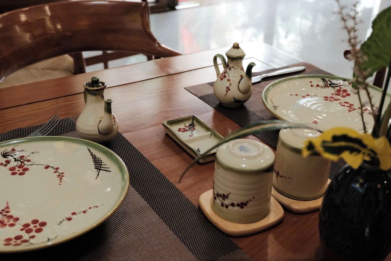 Una mesa de comedor dispuesta con platos, una tetera, una taza y un pequeño jarrón con una planta.