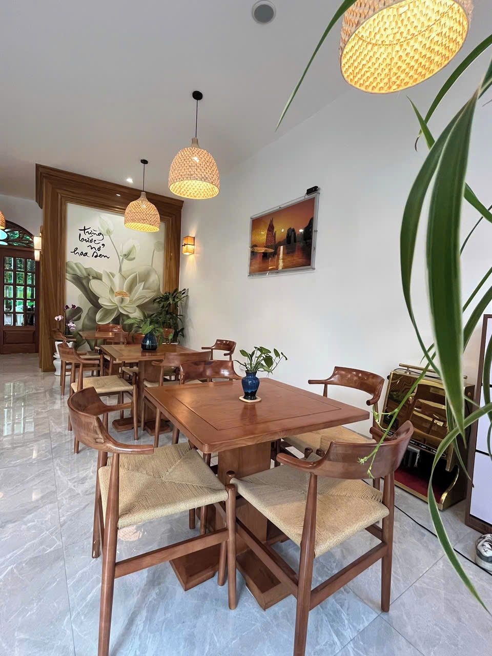 Un comedor con una mesa y sillas de madera, lámparas colgantes y una pared con un mural floral.