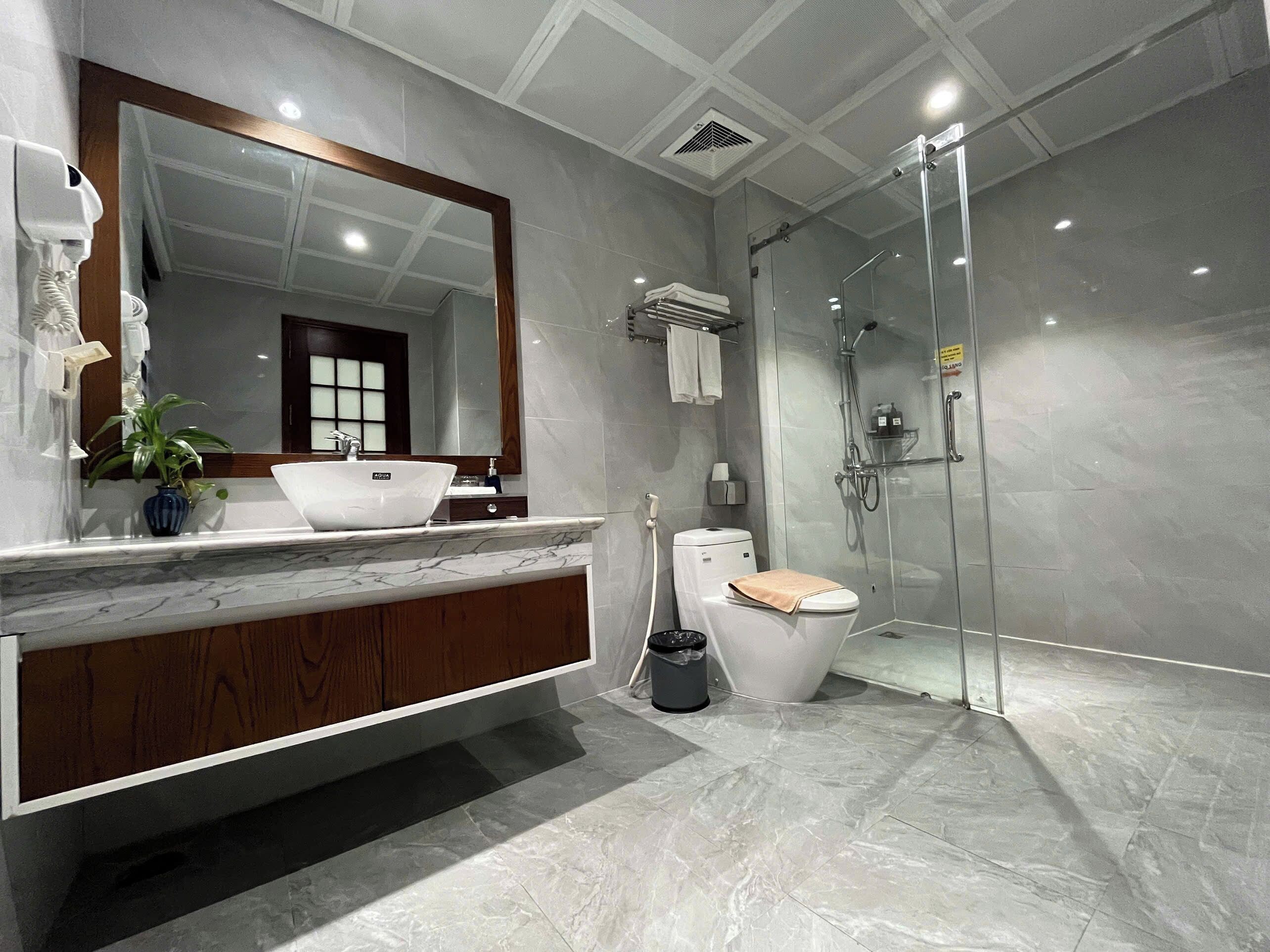 A modern bathroom with a marble sink, a large mirror, a toilet, and a glass-enclosed shower.
