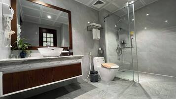A modern bathroom with a marble sink, a large mirror, a toilet, and a glass-enclosed shower.