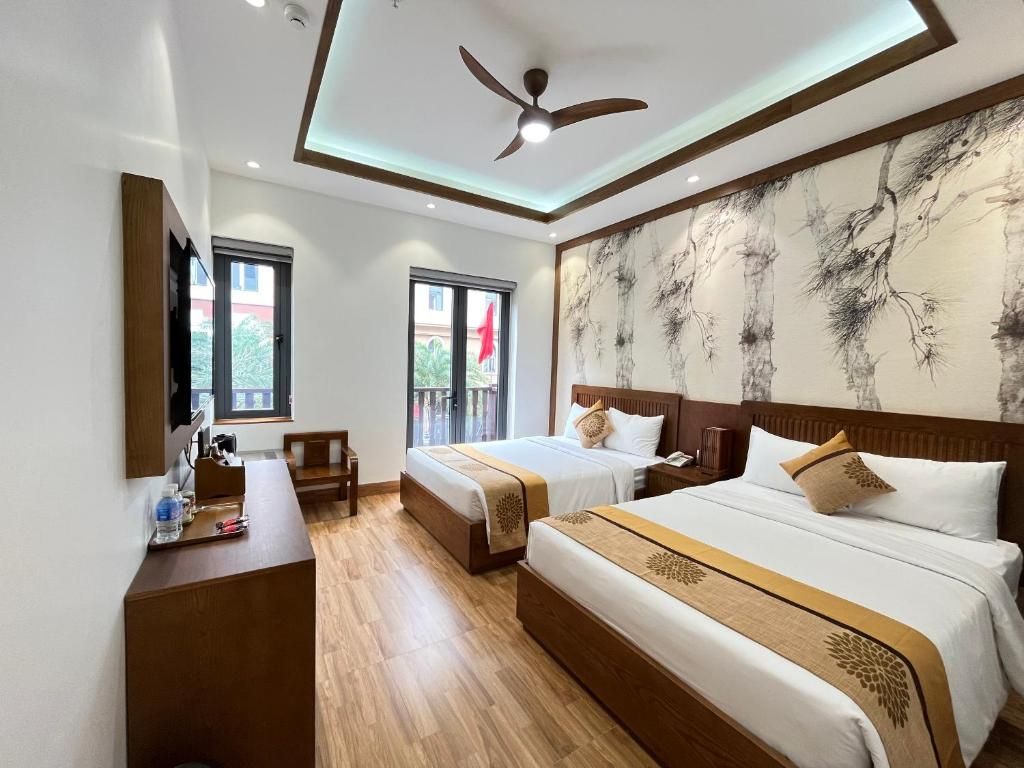 Quarto de hotel com duas camas, uma escrivaninha e um ventilador de teto.