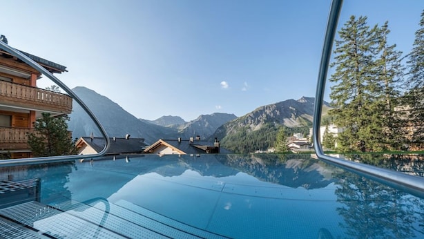 A clear pool with a view of mountains and a wooden building. - Wadhotel National (Arosa)