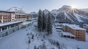 A hotel with multiple floors, a parking area, and a view of snow-covered mountains. - Wadhotel National (Arosa)