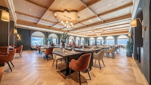 A spacious dining area with multiple tables and chairs, wooden flooring, and a high ceiling with exposed beams. - Wadhotel National (Arosa)