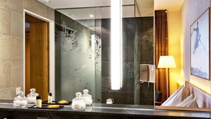 A modern bathroom with a large mirror, two sinks, a shower, and a towel rack. - Wadhotel National (Arosa)